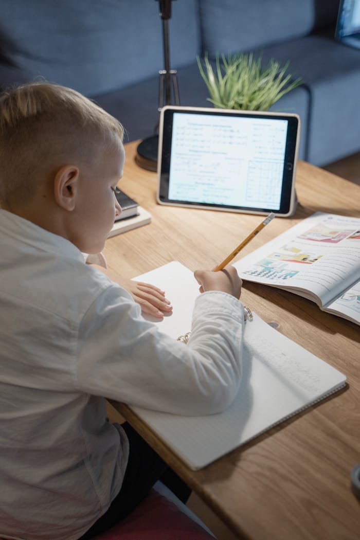 Young boy focuses on studying at home using a tablet and notebook, fostering an educational environment.